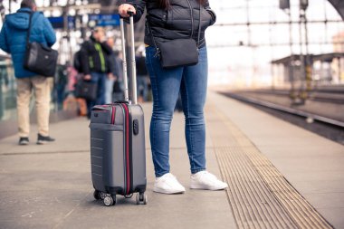 Küçük el bagajlı güzel bir kadın tren istasyonunda tren ve ulaşım konseptini bekliyor.