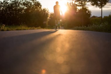 Güzel yaz günbatımında bisiklet yolunda paten kaymaktan hoşlanan genç bir adam. Yaşam tarzı ve spor anlayışı.