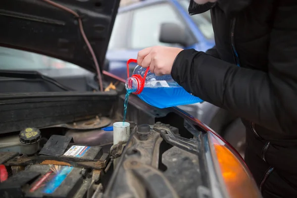 Detail on pouring anti-freeze liquid screen wash into dirty car from blue anti-freeze water container, car concept