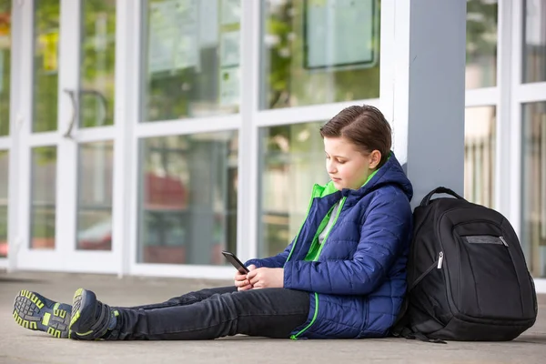 Schulschwänzer-Konzept, kleiner Junge bleibt der Schule fern und spielt Spiele auf Handy oder Smartphone, Abwesenheit von der Schule — Stockfoto