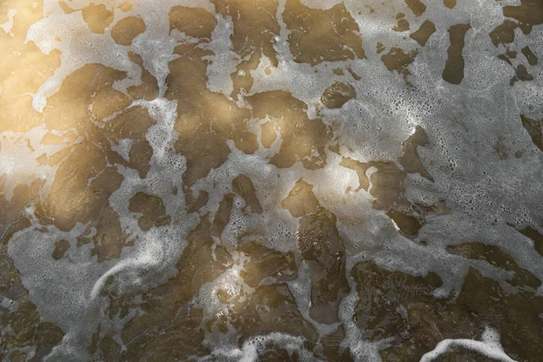 Морська вода і біла піна на пляжі в золотому сонці, жовтий пісок. — стокове фото
