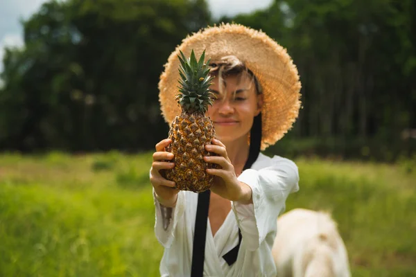 Mädchen mit Ananas in der Hand, in weißem Kleid und Strohhut — Stockfoto