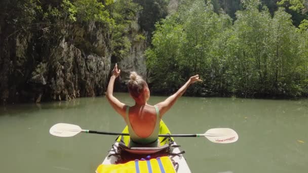 Uma menina está nadando em um caiaque de mar com remos entre a selva — Vídeo de Stock