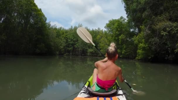 一个女孩带着桨在一艘海上皮划艇上在丛林中游泳 — 图库视频影像