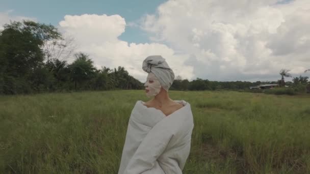 Chica con máscara envuelta en una manta y de pie al aire libre en el campo — Vídeos de Stock