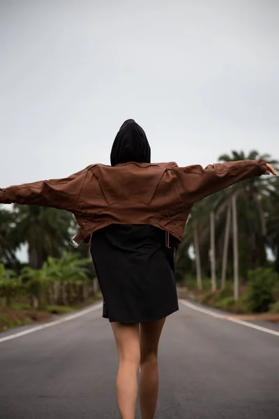 Chica en una chaqueta de cuero marrón está en un camino pavimentado —  Fotos de Stock