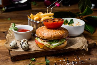 Domates soslu hamburger ve patates kızartması, ahşap bir masada, restoranda servis ediliyor.