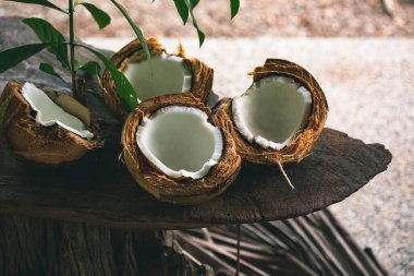 Ahşap bir masada kırılmış hindistan cevizleri ve yakın avuçlarında yapraklar.