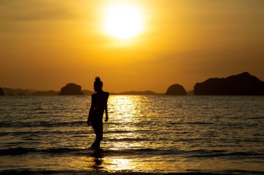Sahilde bir kızın silueti, denizin ve gün batımının arka planında.