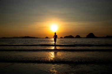 Sahilde bir kızın silueti, denizin ve gün batımının arka planında.