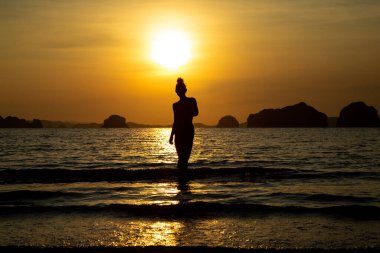 Sahilde bir kızın silueti, denizin ve gün batımının arka planında.