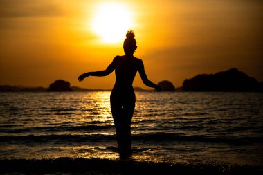 Sahilde bir kızın silueti, denizin ve gün batımının arka planında.