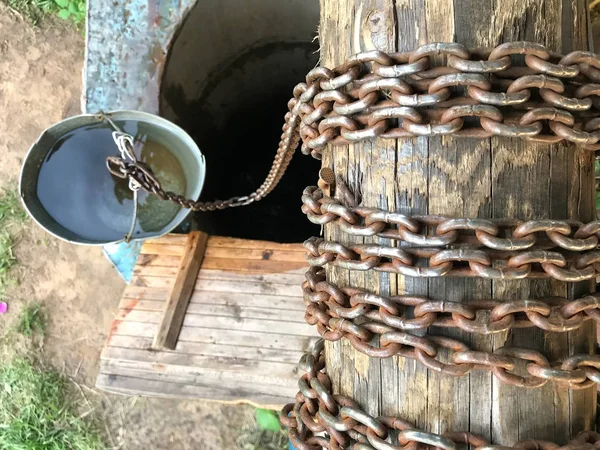 Draufsicht auf einen alten Brunnen. Im Vordergrund befindet sich eine Ankerwinde mit einer Stahlkette. Im Hintergrund steht ein Eimer Wasser. — Stockfoto