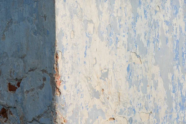 Corner of the wall of an old house. The wall is covered with plaster. Blue paint has scuffs and scratches. Background. Texture.