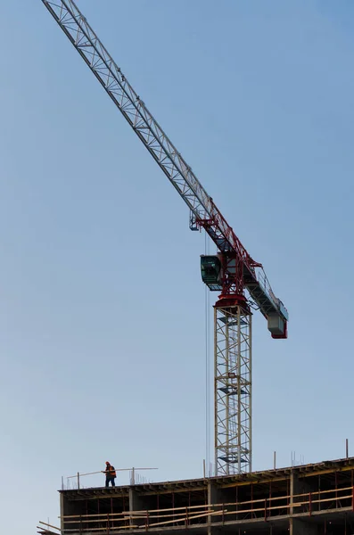 Landscape construction of a large building. There is a tall construction crane and building frame. A small human figure does the work in the lower left corner of the frame. Background. Decoration.