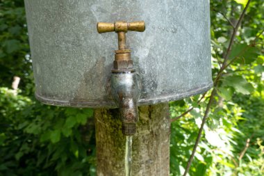 Pirinçten bir musluğa yakın çekim ve akan su. Bu galvanize çelikten yapılmış bir lavabo. Arkaplan.