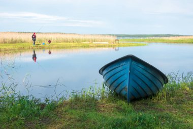 Göl kenarında sakin bir deniz manzarası. Uzakta kıyıda bir balıkçı figürü görülebilir. Önde mavi bir kayık uzanıyor..