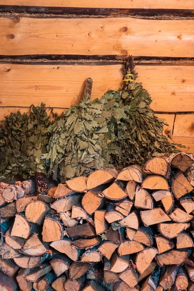 Huş ağacı ve meşe dallarından yapılmış süpürgeler yakacak odun yığınının üzerinde yatıyor. Arka planda bir ahşap duvar görülebilir. Geçmişi. Doku.