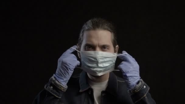 Muž si nasadí masku na tvář na tmavém pozadí a podívá se do kamery — Stock video