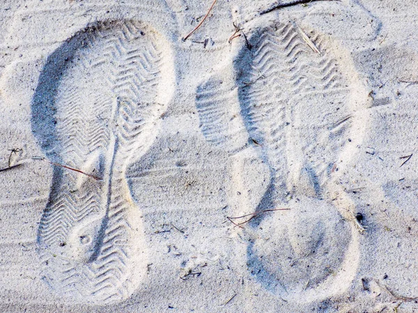 Footprints of shoes imprinted in the sand.
