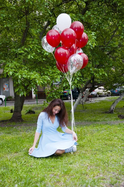 happy woman with party birthday baloons outdoor in summer sitting on green grass. One more step and she will fly