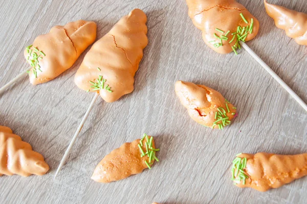 Easter meringue with candy carrots on a sticks and wooden background.