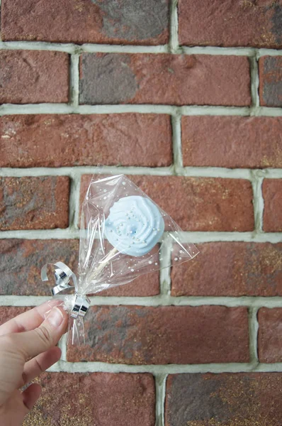 Wrapped candy with transparent cellophane in female hand on brick wall background, copy space