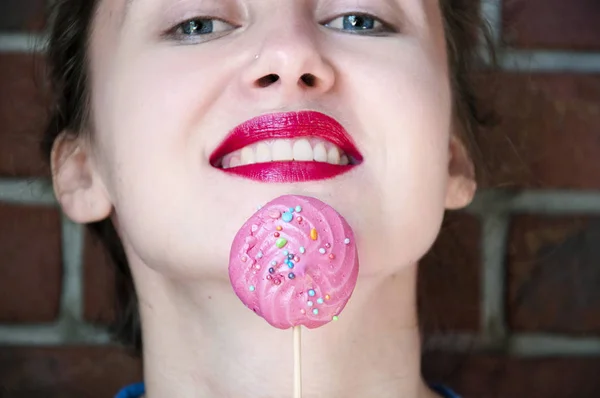 Beauty fashion model girl with colourful makeup taking colorful meringue lollipop. Beautiful woman, bright make-up. Purple lipstick. Diet,dieting concept. Sweets.