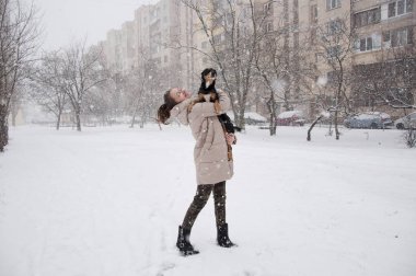 Oldukça sevimli genç kız ya da seksi kadın bej kışın gülümseyen ceket ve askeri kot pantolon doğal beyaz zemin üzerine karlı soğuk kış kar ve kar taneleri ile siyah köpek ya da köpek yavrusu evde beslenen hayvan duruyor kamuflaj