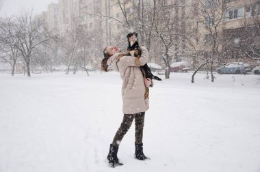 Oldukça sevimli genç kız ya da seksi kadın bej kışın gülümseyen ceket ve askeri kot pantolon doğal beyaz zemin üzerine karlı soğuk kış kar ve kar taneleri ile siyah köpek ya da köpek yavrusu evde beslenen hayvan duruyor kamuflaj