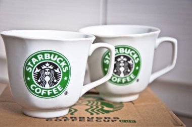 Kiev, Ukraine - February 16, 2016: Two ceramic shiny company white cups with stylish round green logo of Starbucks coffeehouse corporation on paper box clipart