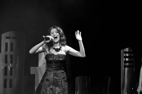 Elegant young female singer in black dress holding microphone, live performance, concert, unrecognizable person. black and white