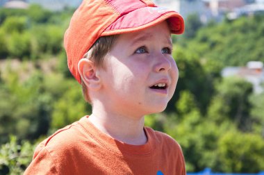 sevimli küçük bir bebek veya çocuk kırmızı bere ve turuncu gömlek güneşli yüzüne ağlıyor ile yaz aylarında doğal yeşil ağaçlar arka plan üzerine açık