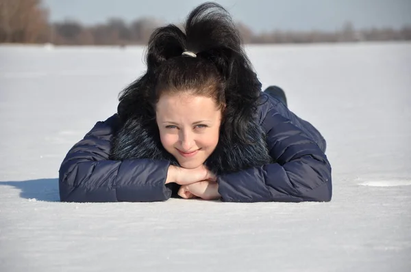 漂亮可爱的年轻黑发女孩在蓝色冬衣与毛皮阳光寒冷的冬天天在自然白色背景铺设在雪 — 图库照片