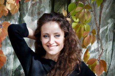 genç seksi kadın veya kız Güz mevsimlik oldukça mutlu gülümseyen yüzünde uzun esmer kıvırcık saçlı asma veya üzüm açık ahşap veya ahşap arka plan üzerinde renkli güneşli sarı ve turuncu kırmızı yaprakları