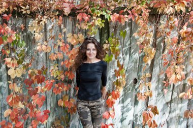 siyah gömlek ve kamuflaj kot renkli sonbahar yaprakları yakınında uzun saçlı Genç seksi kadın veya kız güzel mutlu gülümseyen yüz ahşap veya ahşap arka planda asma veya üzüm güneşli açık