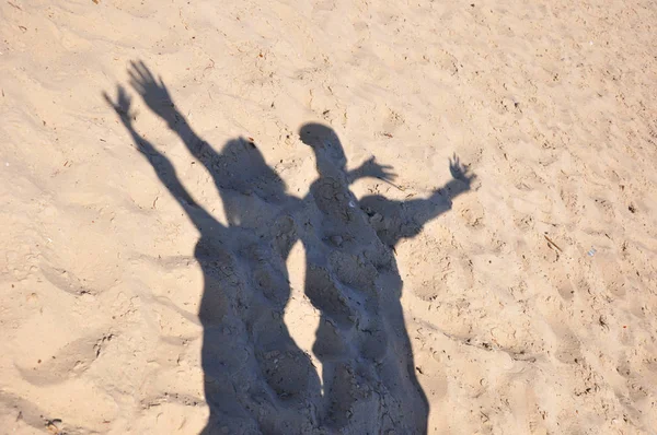 shade or shadow of young happy couple of people male and female with emotional raised hands sunny day outdoor on summer sand