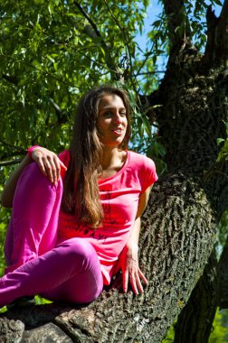 genç seksi kadın veya kız oldukça sevimli yüz ve ağaç gövdesi yeşil pembe gömlek oturur uzun esmer saçlar ile güneşli yaprakları doğal zemin üzerine açık