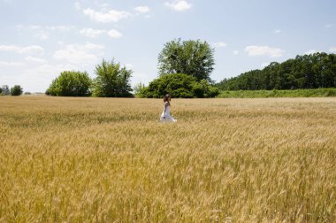 Genç bir kadın güneşe doğru yürüyor. Doğada yürüyen rüya gibi bir kadın. Baharın tadını çıkarıyor. Yaz günbatımında buğday tarlasında yürümek. Seyahat konsepti, huzur verici rahatlama anı. Mutlu Toprak Günü.