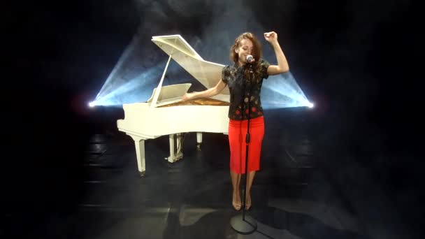 レトロな女性歌手がスポットライトと白いピアノと音楽でステージ上でマイクでジャズを歌う — ストック動画