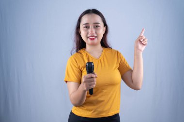 Sarı tişörtlü, gülümseyen bir kadın mikrofon tutuyor, coşkuyla yukarı bakıyor.