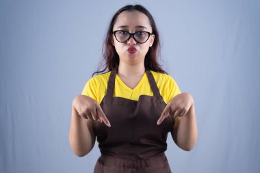 Önlük takan ve gözlüklü bir kadın somurtkan bir ifadeyle aşağıya bakıyor.