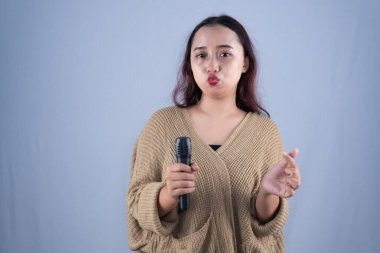 Bir kadın mikrofonu tereddütle tutar, resmi bir ortamda hafif bir huzursuzluk veya isteksizlik taşır.