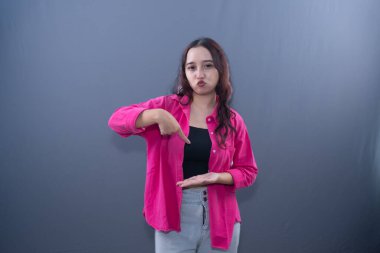 Pembe gömlekli ve kot pantolonlu bir kadın, gri bir arka planda neşeli bir buruşukluk gösteriyor.