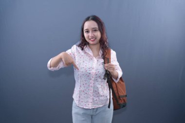 Sırt çantasıyla gülümseyen genç bir kadın resmi, profesyonel bir stüdyo ortamında yer alıyor.