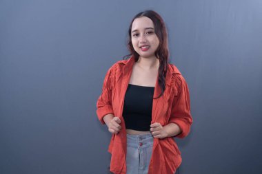 Kırmızı tişörtlü, siyah bluzlu, kendine güvenen genç bir kadın gri bir arka plana gülümsüyor.