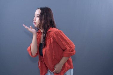 Kırmızı tişörtlü genç bir kadın, profil içinde yakalanır. Gri bir arka plana öpücük kondurur.