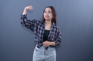 Ekose gömlekli genç bir kadın şakacı pozlar veriyor, kaslarını biraz gergin bir ifadeyle esnetiyor.