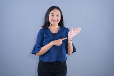 Mavi bluzlu, güler yüzlü genç bir kadın. Güvenle işaret ediyor ve açık elle sunuyor..