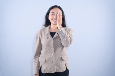 Ceketli, gülümseyen bir kadın bir gözünü eliyle kapatır..